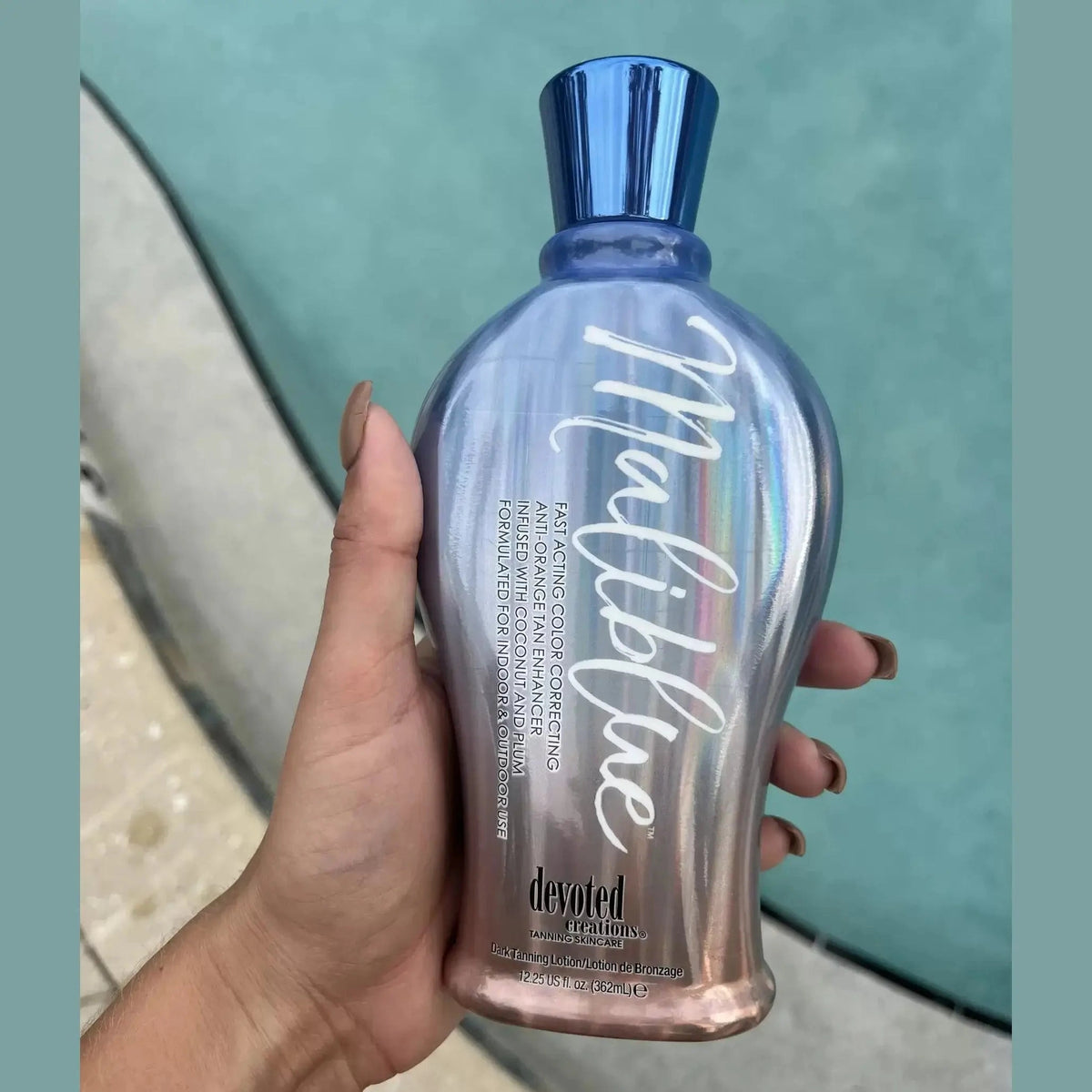 Hand holding Devoted Creations Maliblue hydrating tanning accelerator against turquoise water