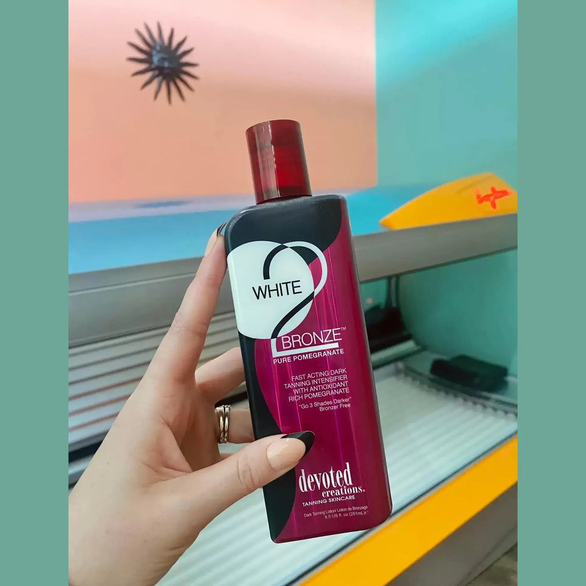 Hand holding Devoted Creations White 2 Bronze dark tanning intensifier near tanning bed