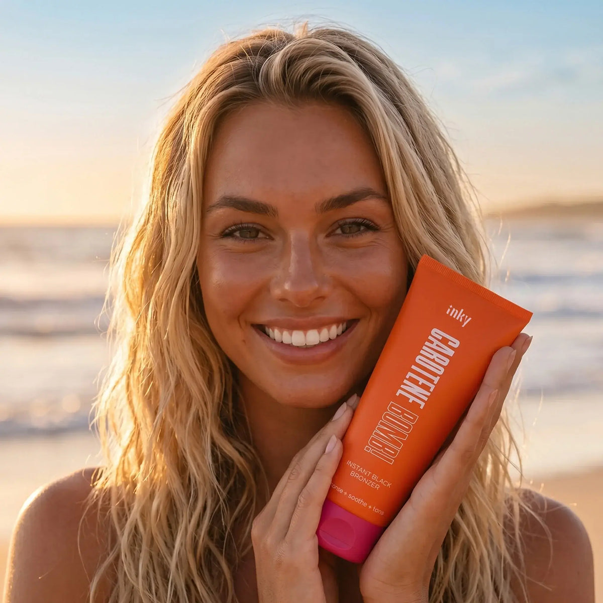 Woman applying Inky Carotene Bomb instant bronzing lotion at beach